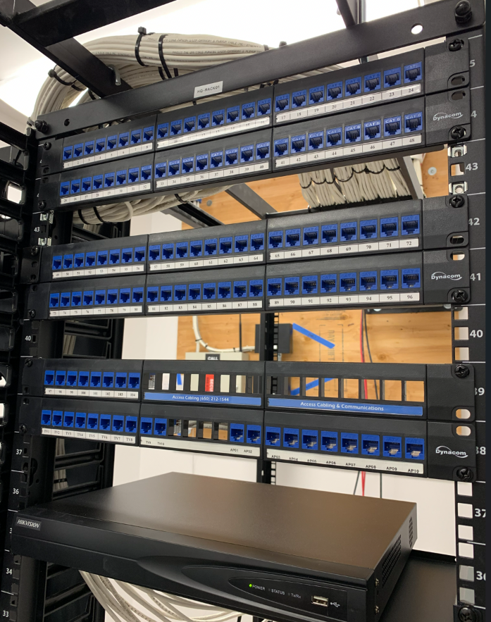 High-density Dynacom Cat6 patch panels labeled for data drops and access points, with a Hikvision NVR mounted below.