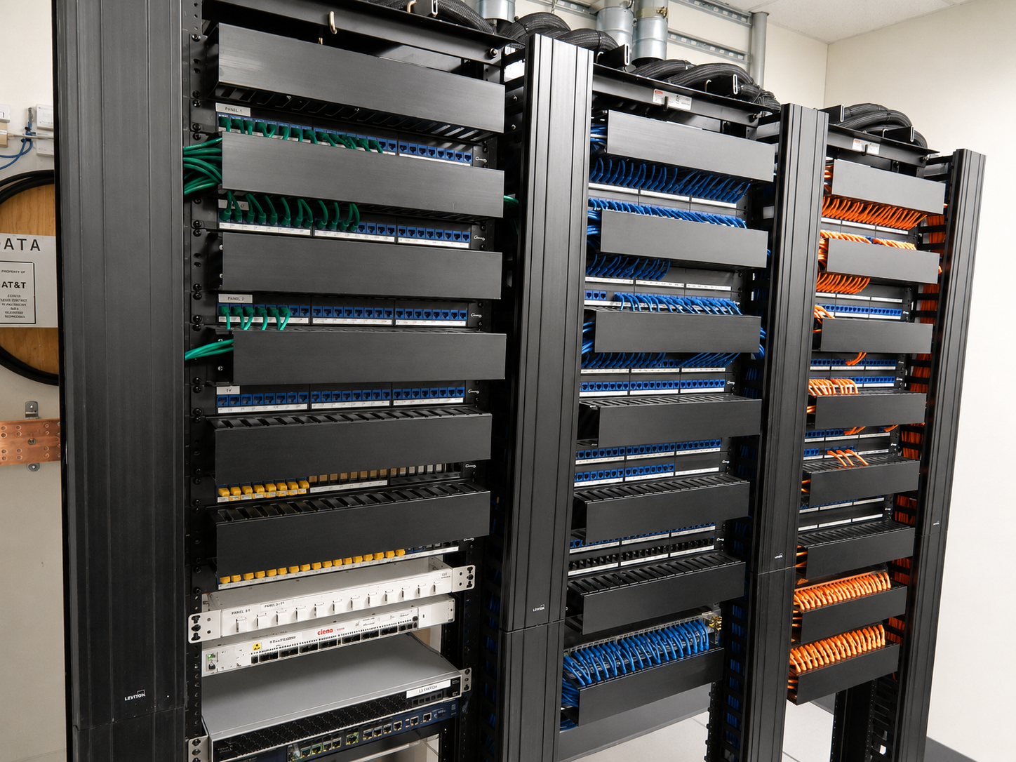 Close-up of three enterprise network racks at Bill.com's Palo Alto headquarters with color-coded Category 6 patch panels — green, blue and orange patch cords — dressed behind horizontal cable management with a Ciena optical transport platform and Leviton hardware installed by Access Cabling.