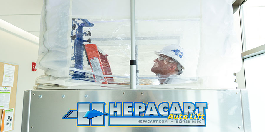 Worker inside an extended HEPACART AutoLift containment enclosure with a ladder for ceiling work