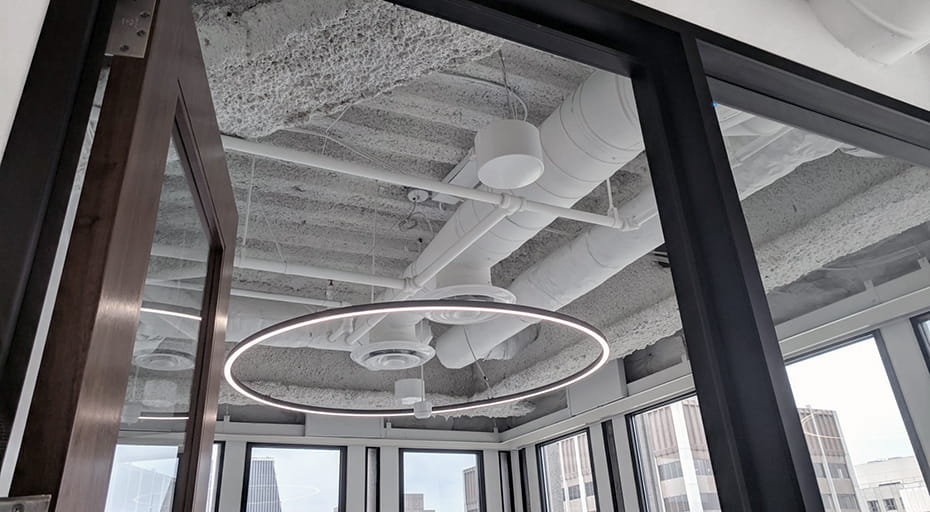 Glass-walled conference room with a ring pendant light and sound masking emitters mounted to the exposed concrete ceiling