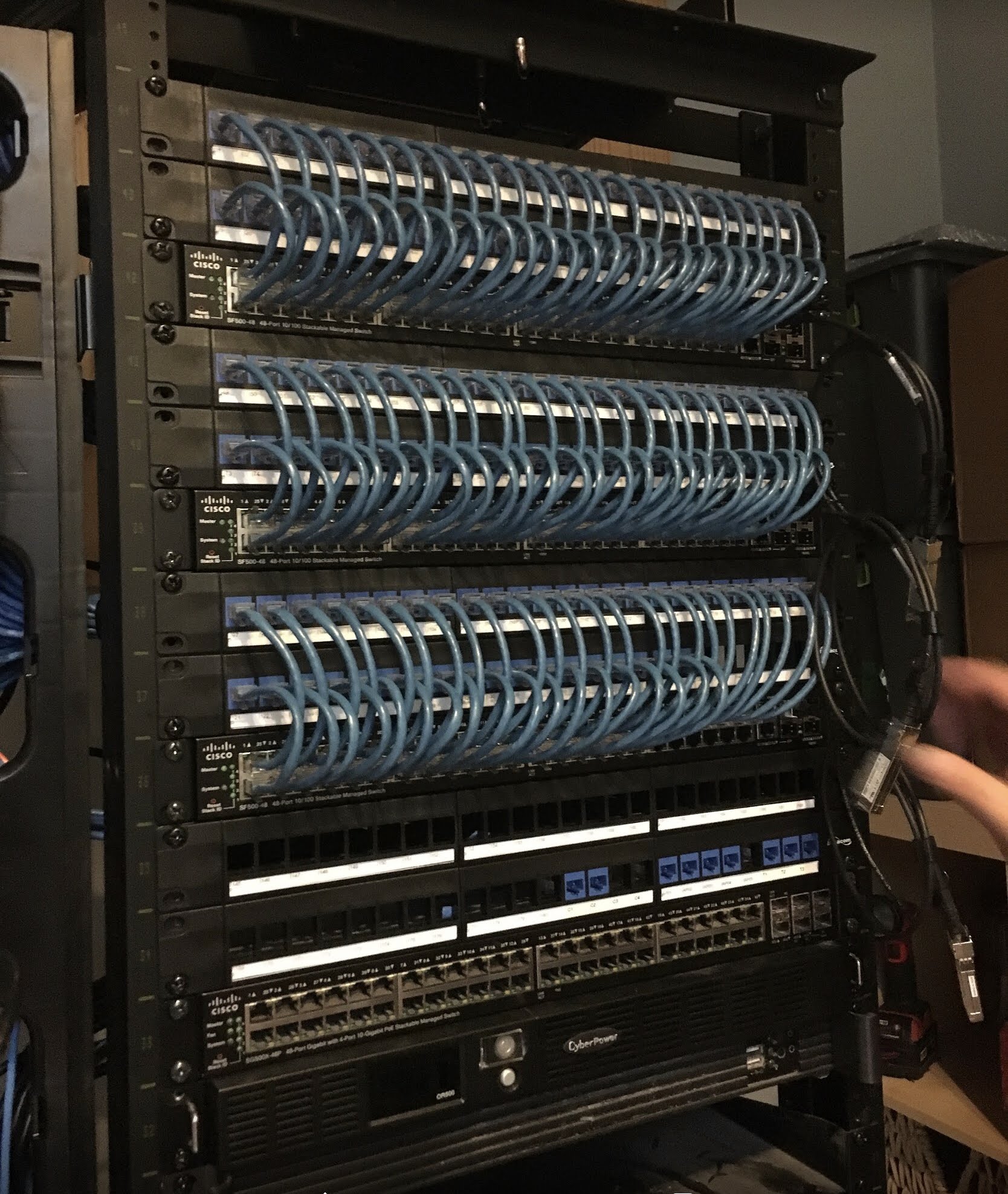 Stack of Cisco SF500 PoE switches with coiled blue Cat6 patch cords powering downstream devices.