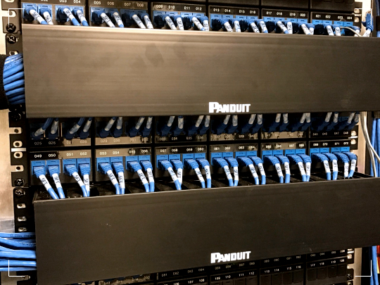 Restaurant-chain IDF rack with densely packed blue Category 6 patch cords across dual Panduit patch panels behind horizontal cable managers — standardized rack build repeated across every location by Access Cabling.
