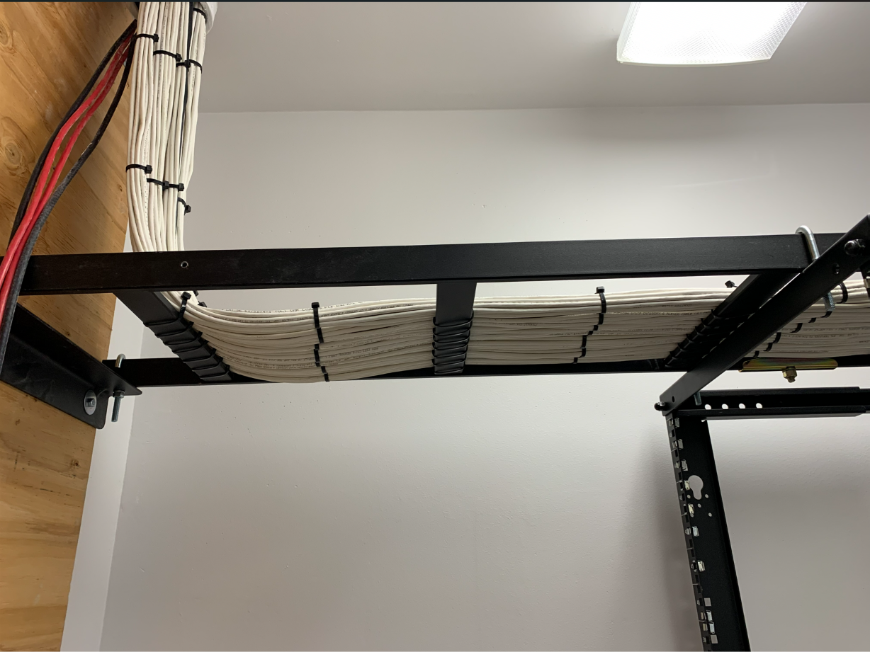 Overhead ladder rack tray carrying a neatly bundled run of Cat6 cabling into the top of a network rack.