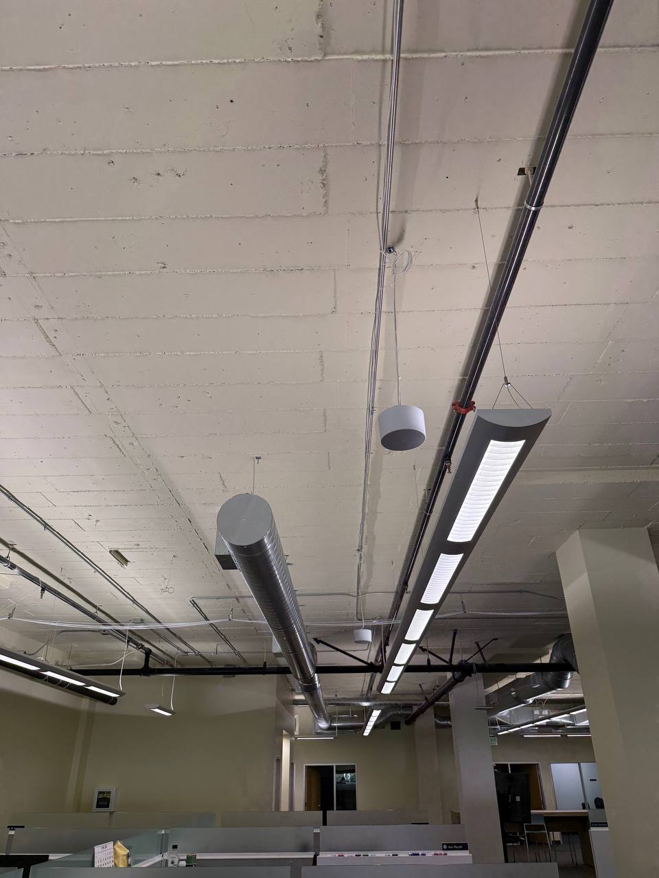 Overhead view of Soft dB SmartSMS-NET sound masking emitters and small white ceiling-mounted sensors distributed among HVAC ducts and conduit in an open-plan California office, installed by Access Cabling.